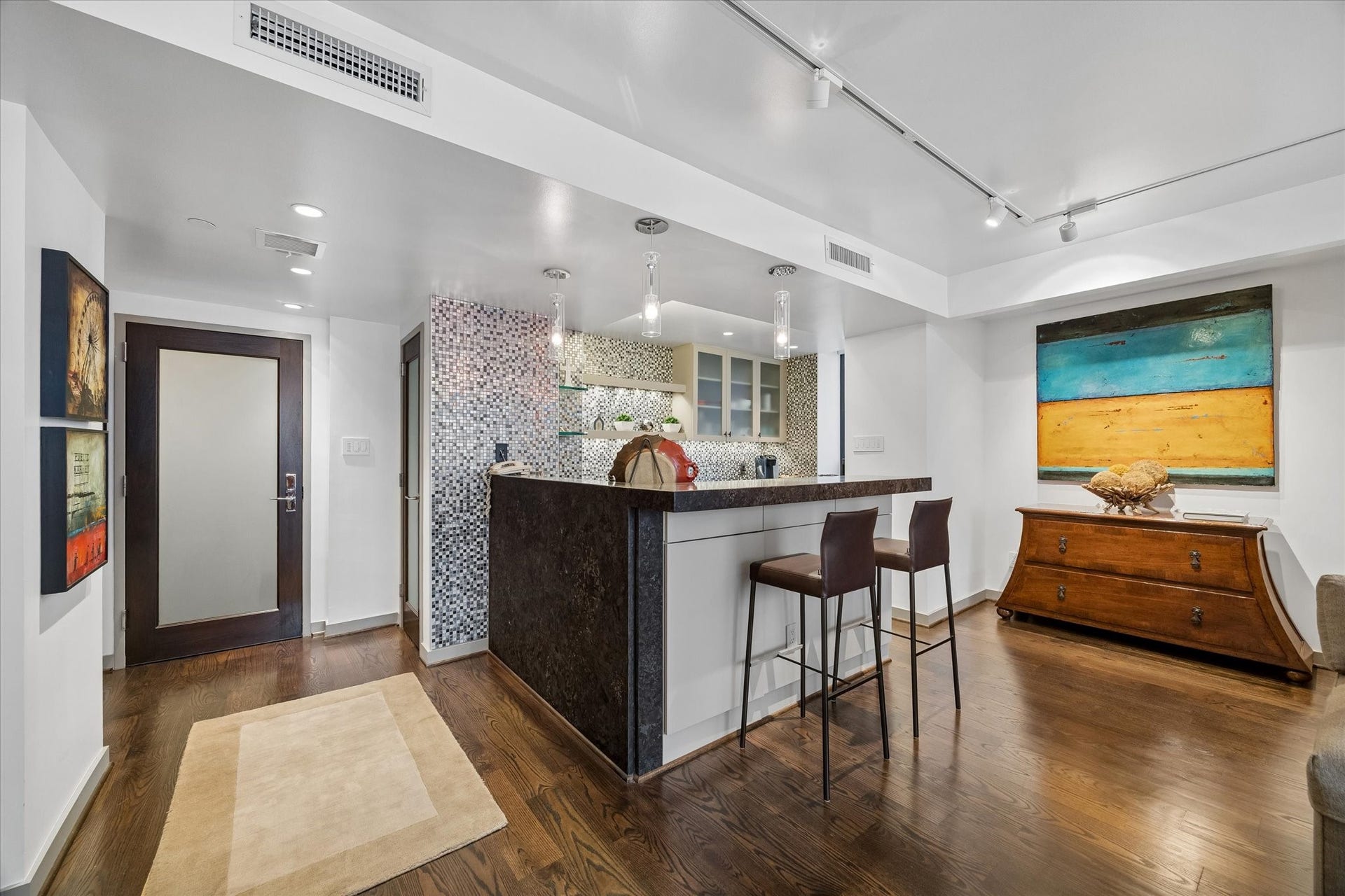 1111 Caroline Street, #2601, Houston, TX 77010 Breakfast bar creates a transition between meal preparation and the living area. Stone counters, mosaic backsplash and glass front cabinetry carry the kitchen finishes across the open plan.