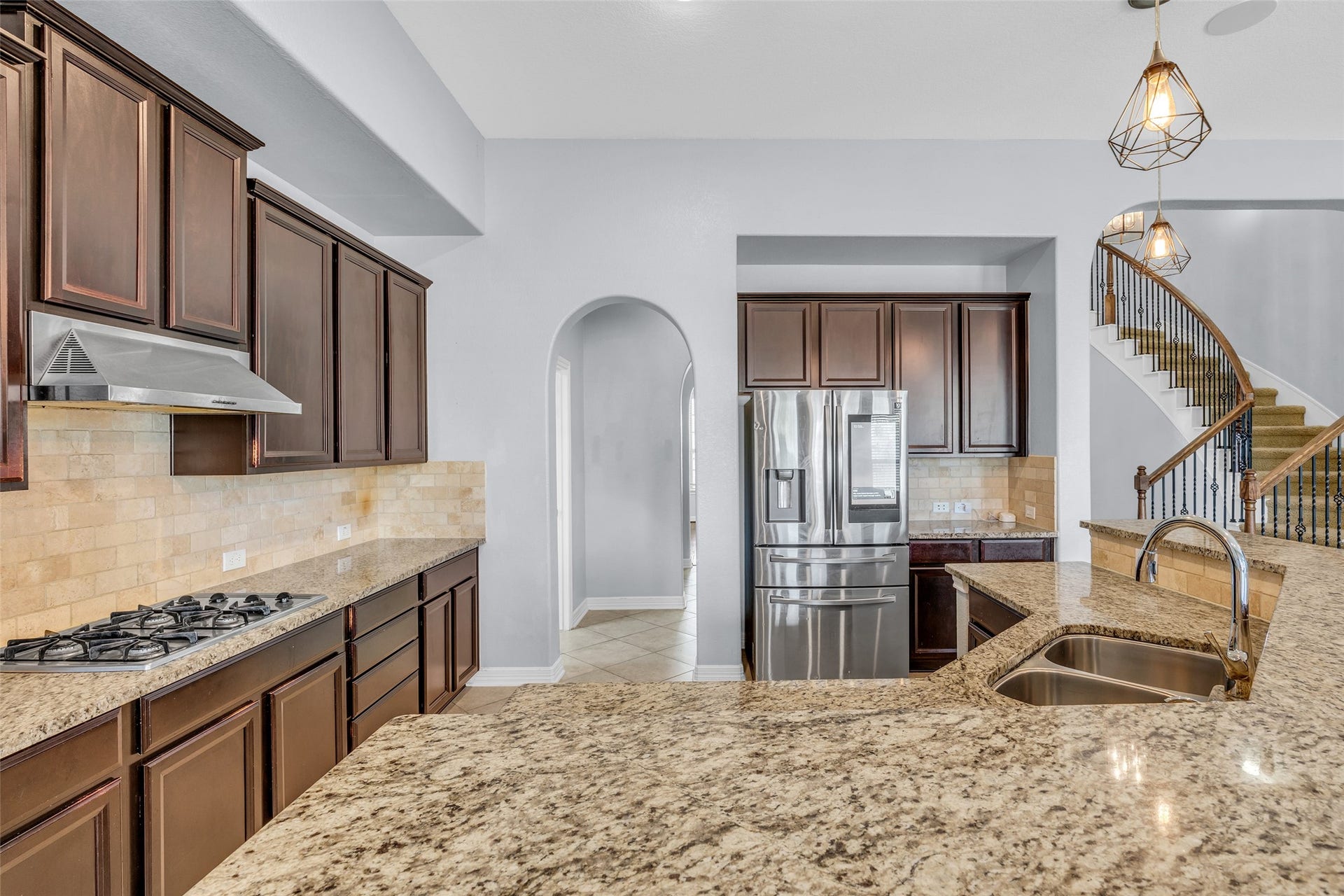 7 Ember Branch Drive, Missouri City, TX 77459 Cook on the gas cooktop under a stainless vent hood, with the curved staircase in view.