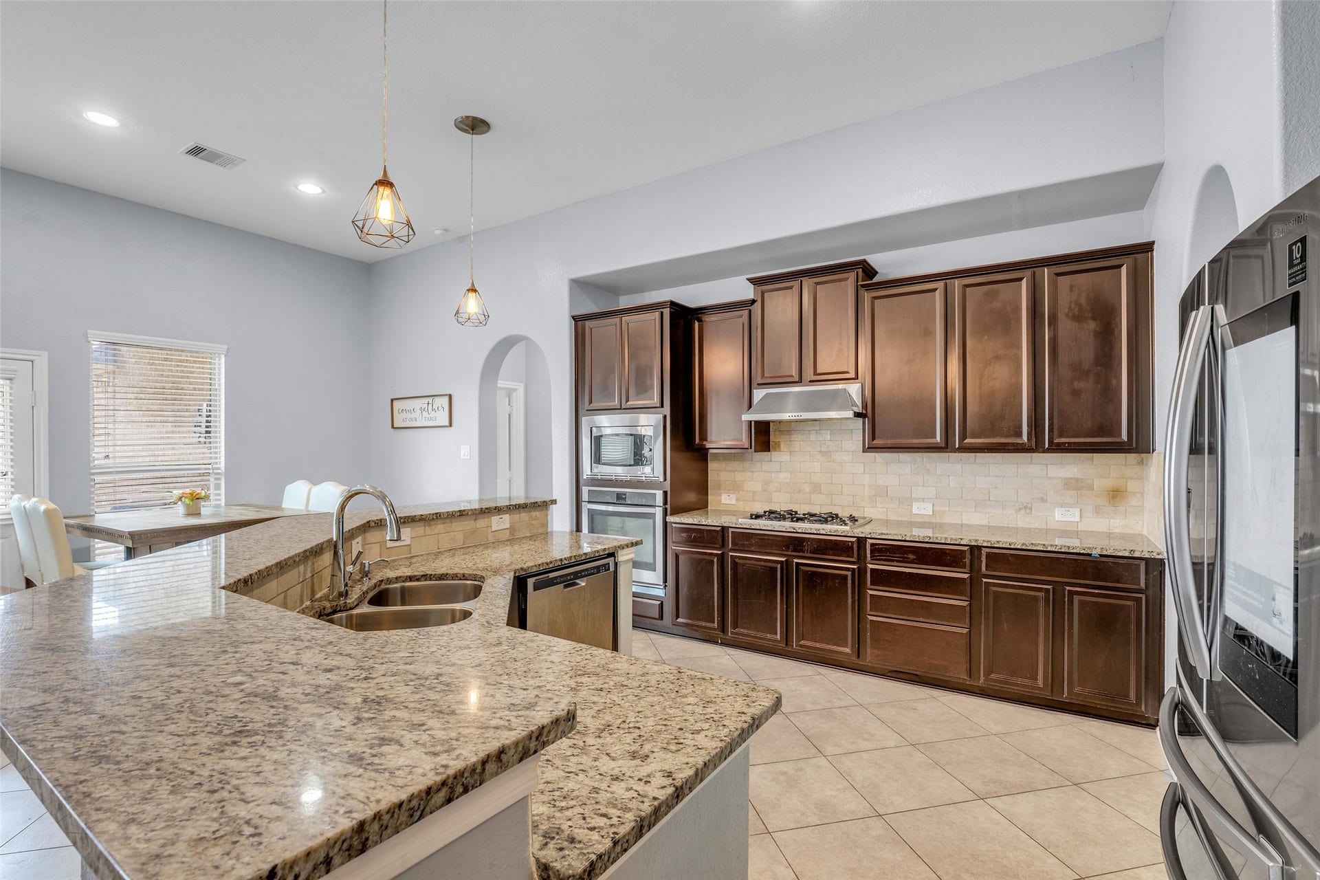 7 Ember Branch Drive, Missouri City, TX 77459 A cook's kitchen with granite countertops, rich wood cabinetry, a tile backsplash and pendant lighting over the island.