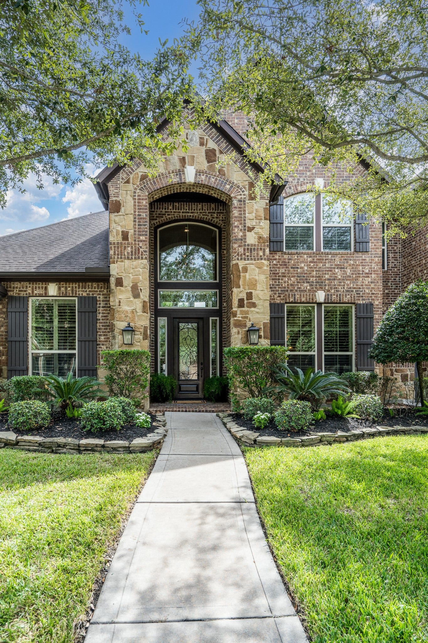 Stone and brick elevation with beautiful, stacked stone landscape and an arched entry welcome all who enter!