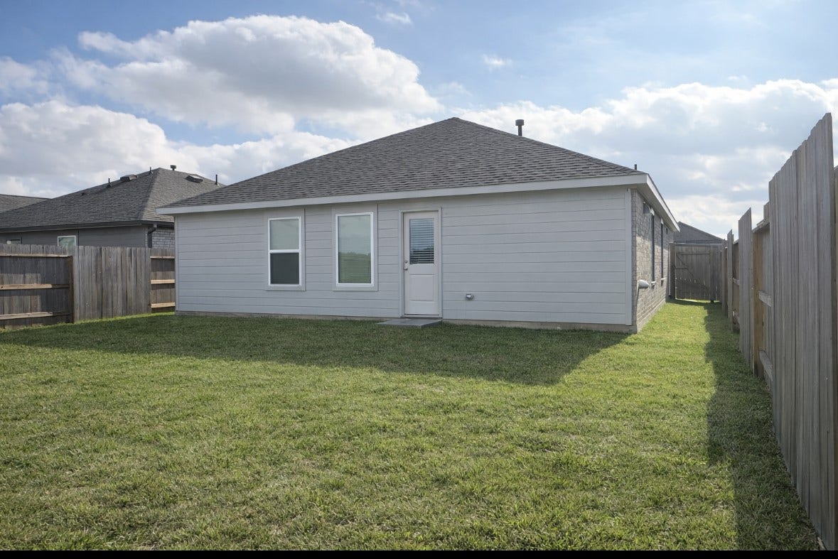 21151 Vercelli, New Caney, TX 77357 A cozy, single-story home with a fenced backyard featuring a well-maintained lawn, perfect for outdoor activities. The exterior is modern with neutral siding and a shingled roof.