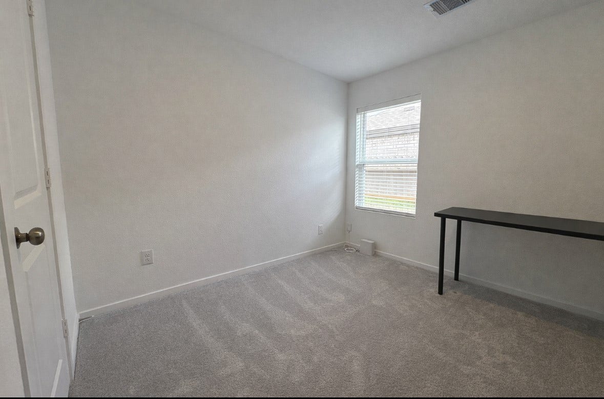 21151 Vercelli, New Caney, TX 77357 Cozy room with neutral walls and carpet, featuring a window that allows natural light. Includes a simple, sleek black table, making it ideal for a home office or study space.
