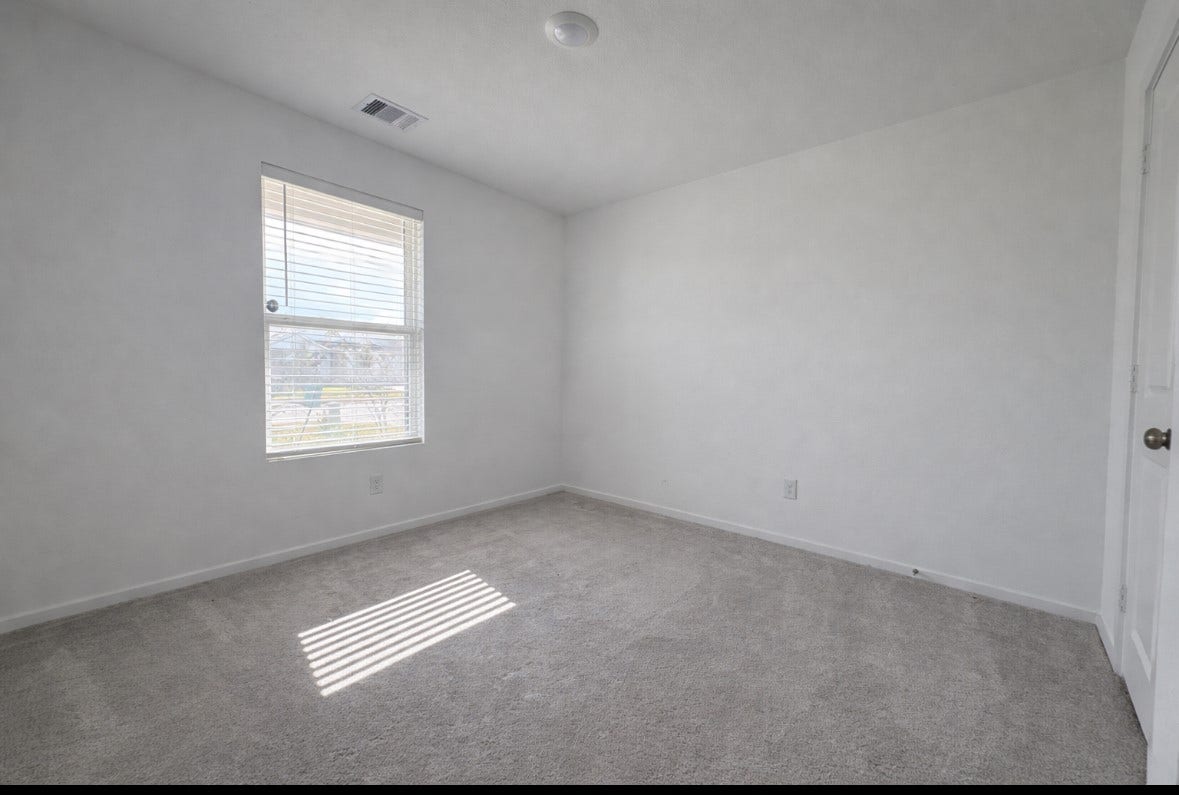 21151 Vercelli, New Caney, TX 77357 This is a bright, empty room with neutral-colored walls and carpet, featuring a window for natural light and a standard door. Ideal for a bedroom or office space.