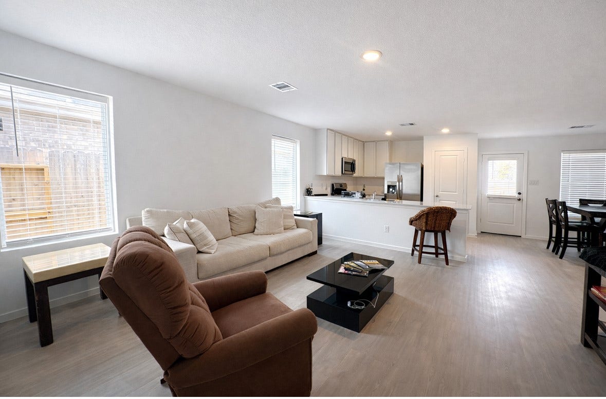 21151 Vercelli, New Caney, TX 77357 This photo showcases a bright and open living space with modern decor. It features a cozy seating area, a sleek kitchen with stainless steel appliances, and a dining area. Large windows allow natural light to fill the room, creating a welcoming atmosphere.