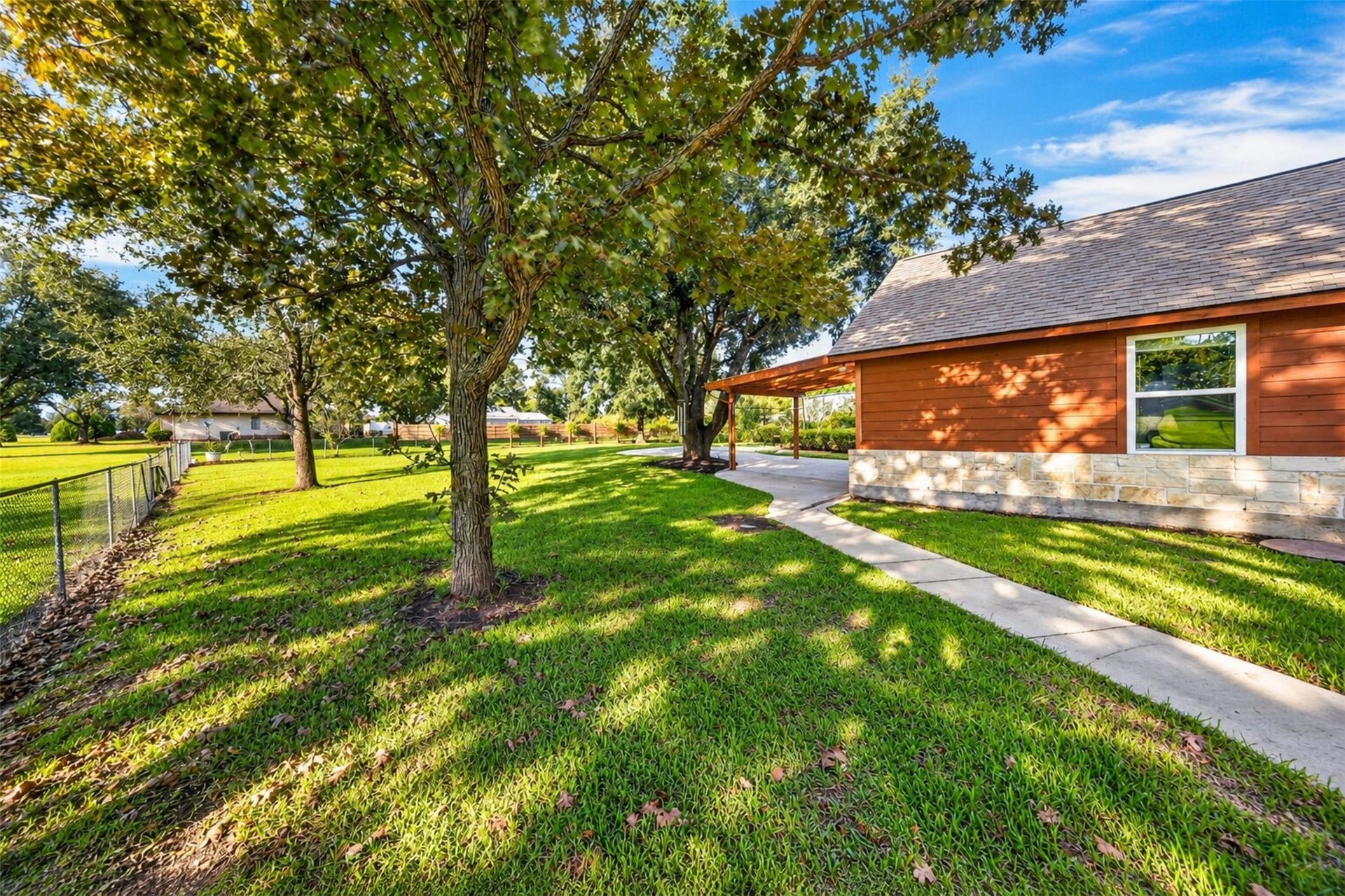 Tree-shaded side yard with chain-link fencing and a walkway leading to the rear patio.