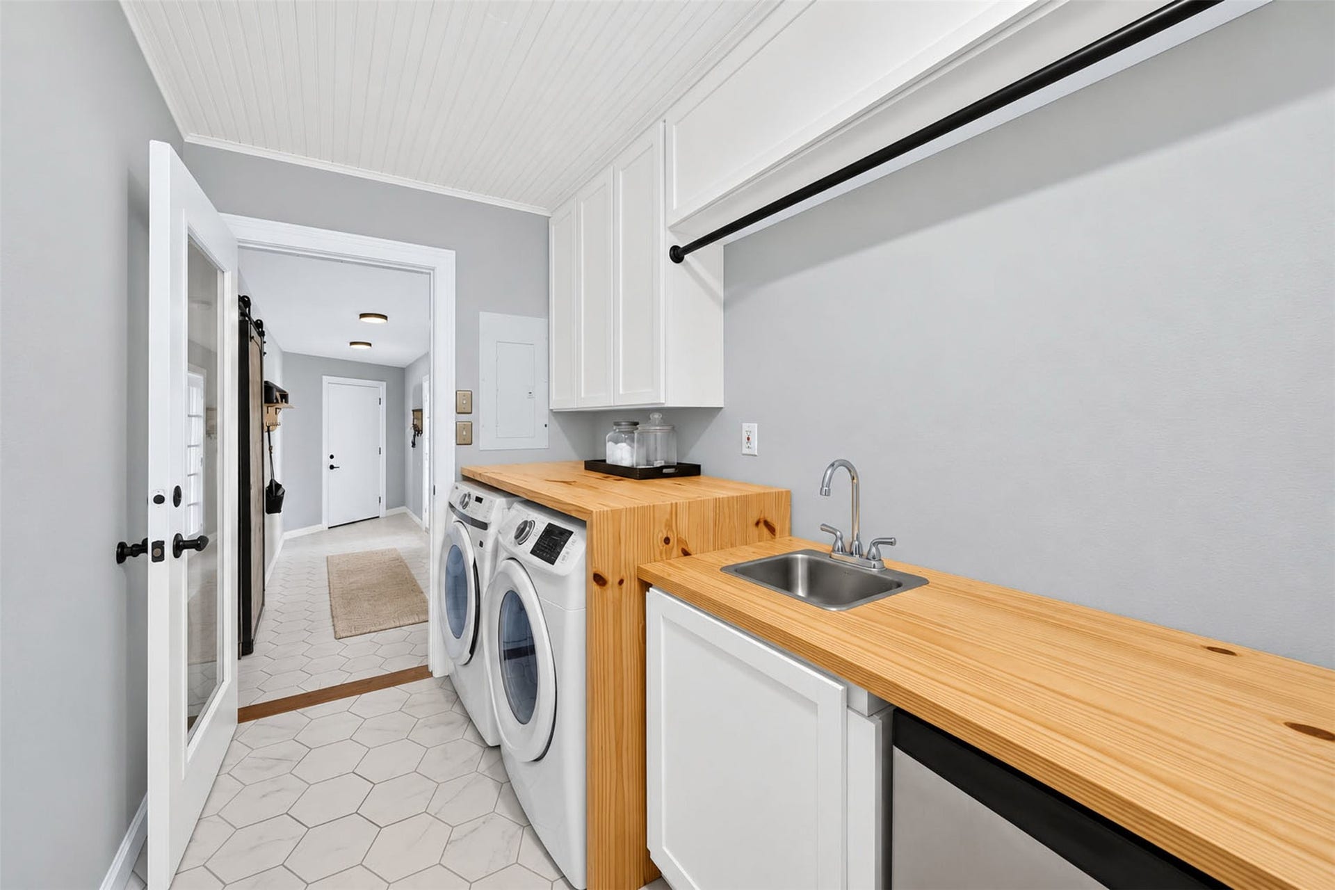 Laundry room offers wood countertops, a utility sink, overhead cabinets, a hanging rod, and hexagonal floor tile.