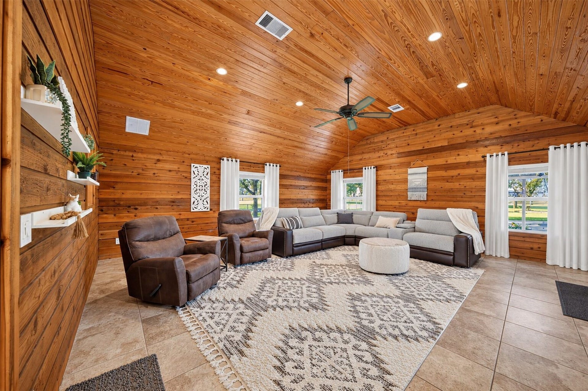 Living room features wood-paneled walls, a vaulted wood ceiling, recessed lighting, and multiple windows overlooking the grounds.