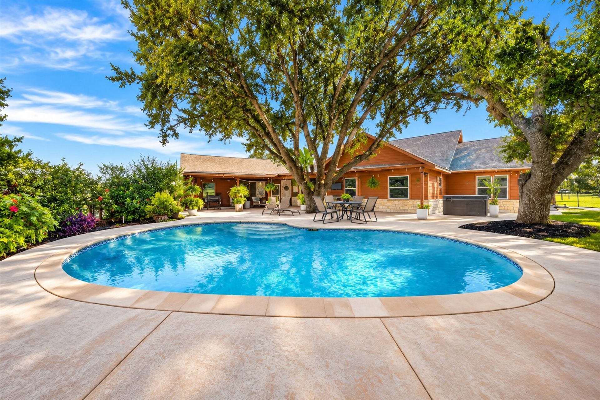Curved pool with entry steps, a surrounding concrete deck, and adjacent covered patio.