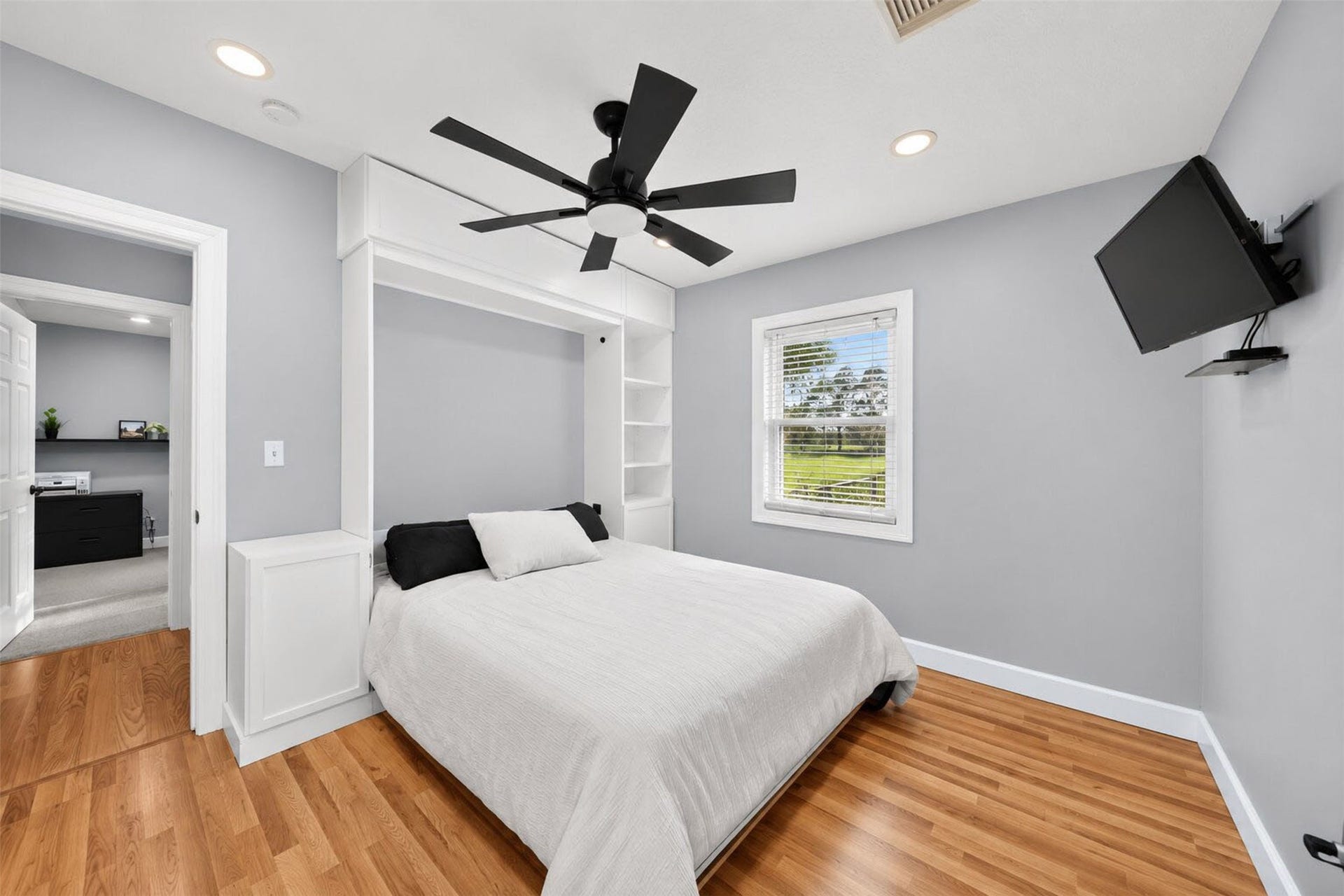 Alternate bedroom view highlights white cabinetry and shelving framing the bed, with a window overlooking the lawn.
