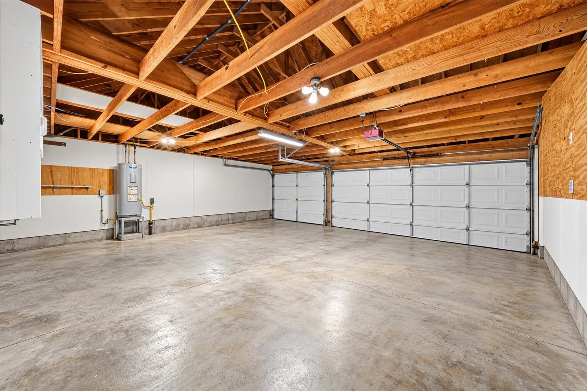 Attached garage interior with concrete flooring, exposed ceiling framing, and double and single overhead doors.