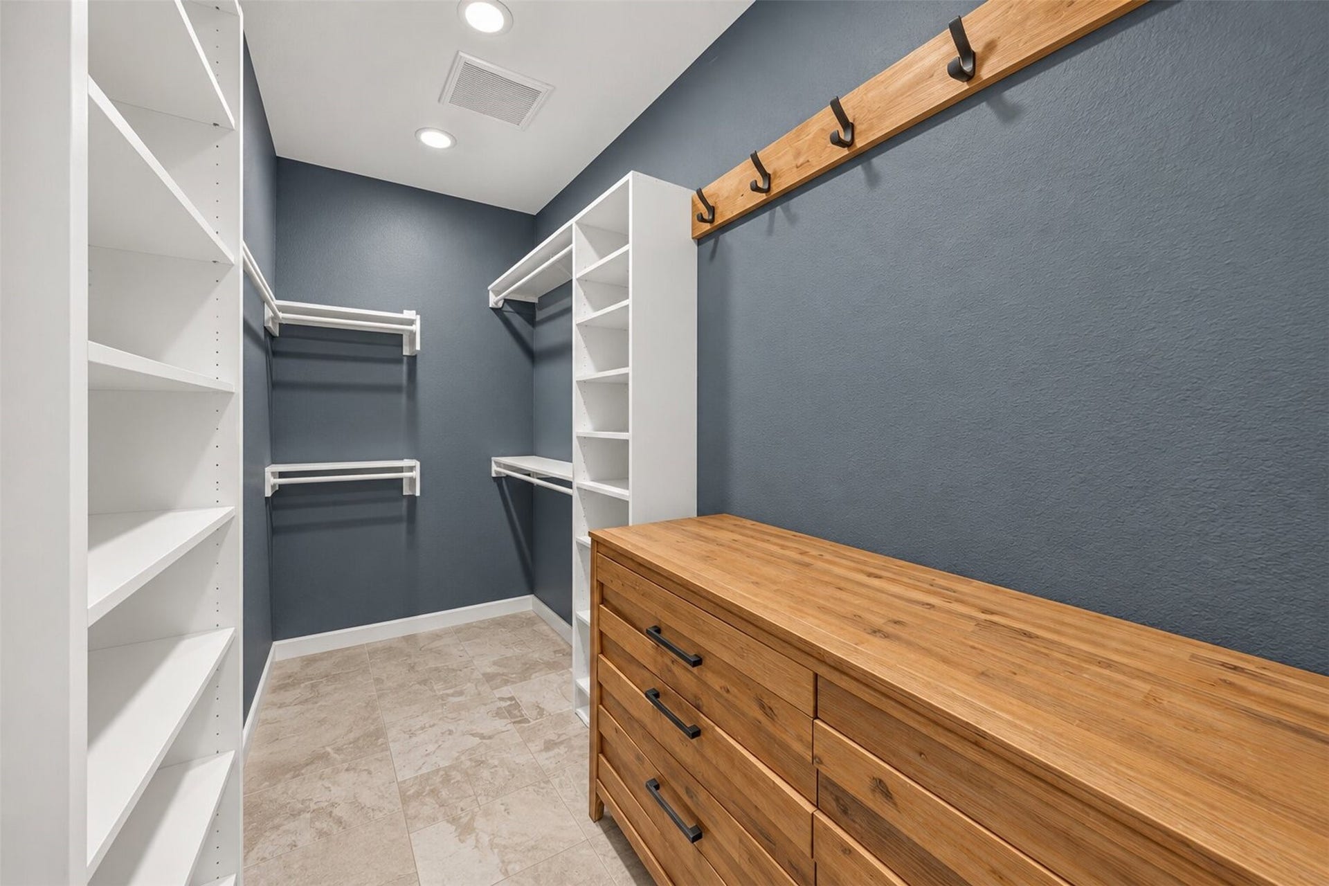 Walk-in closet with open shelving, multiple hanging rods, wall hooks, and tile flooring.