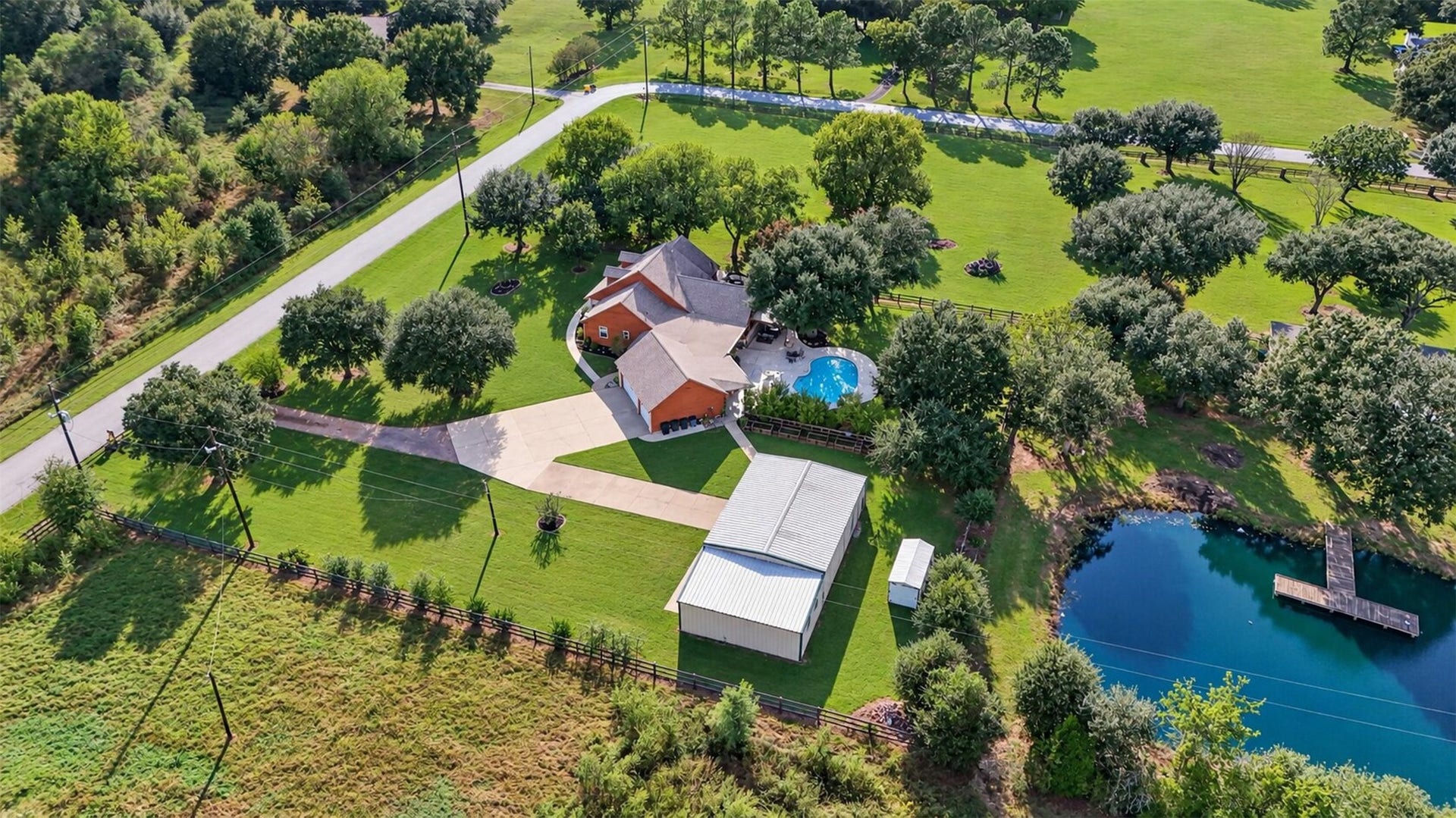 Rear aerial perspective highlights the pool, detached metal building, garden beds, and connecting walkways.