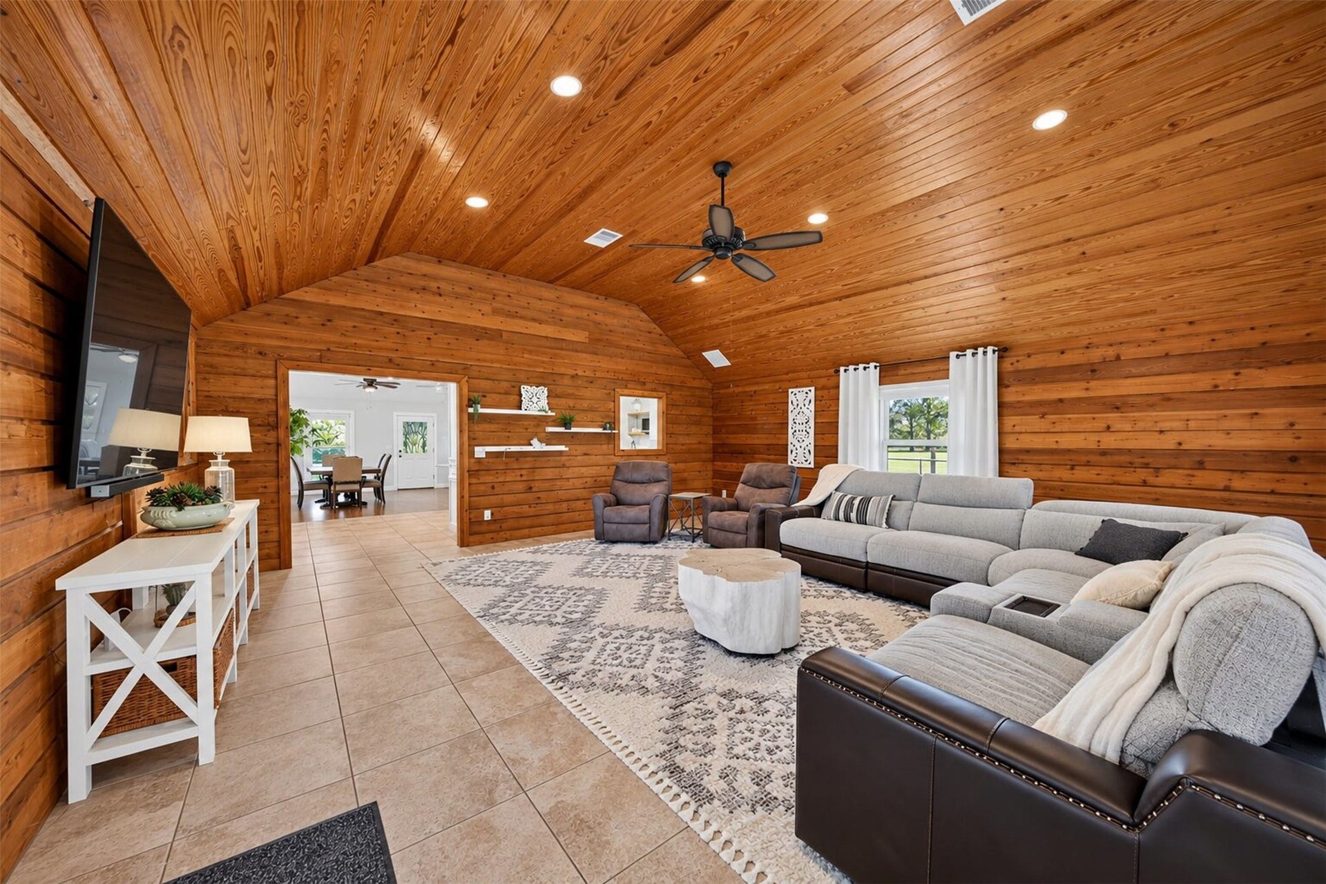 Additional living room view highlights tile flooring, a vaulted wood ceiling, and a wide opening to the dining area.