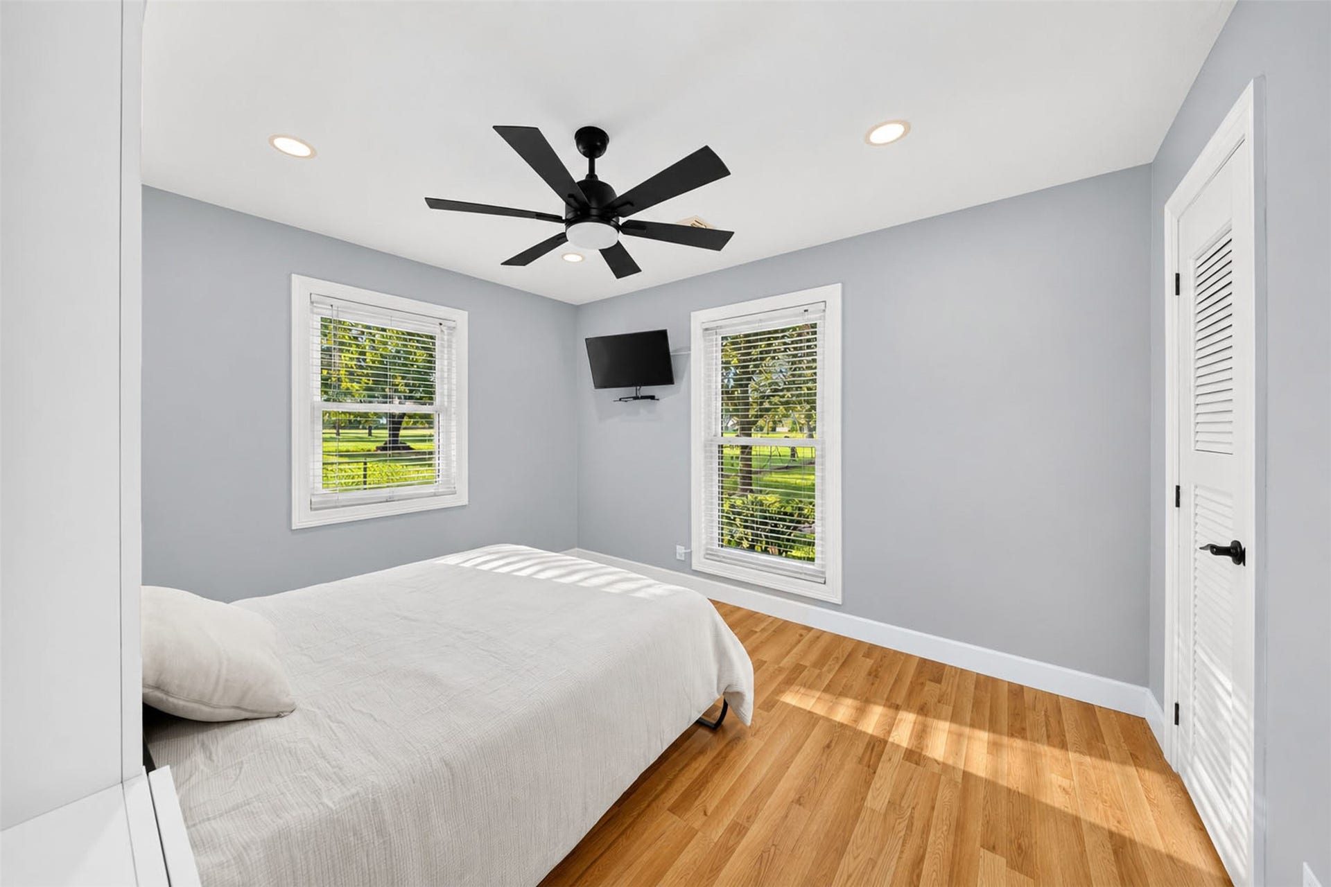 Bedroom with two windows overlooking the grounds, wood-look flooring, recessed lighting, and a ceiling fan.