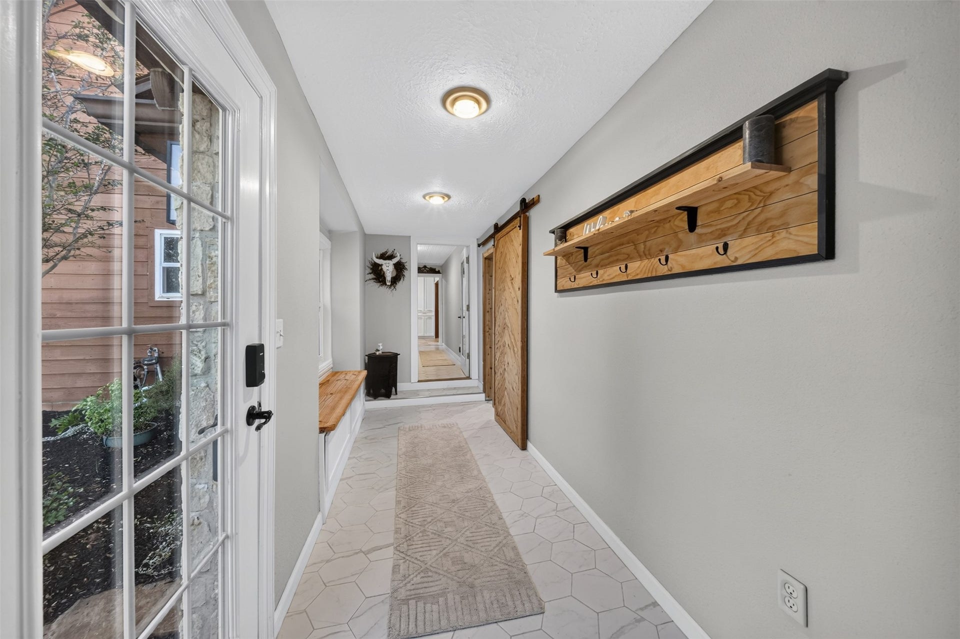 Entry hallway features hexagonal tile flooring, wall-mounted coat hooks, a storage bench, and a wood sliding door.