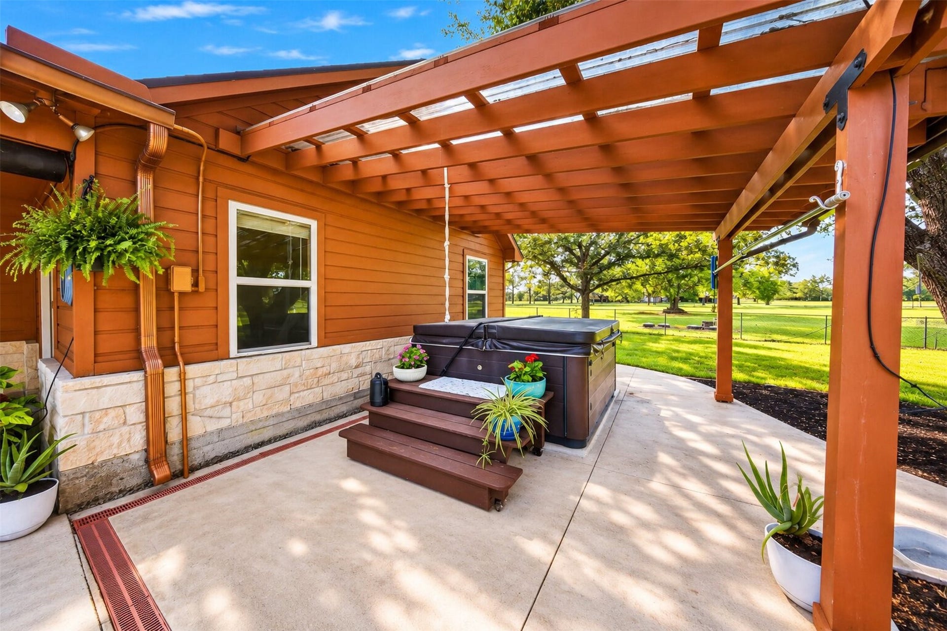 Covered outdoor area with a hot tub pictured, access steps, and views across the tree-shaded lawn.