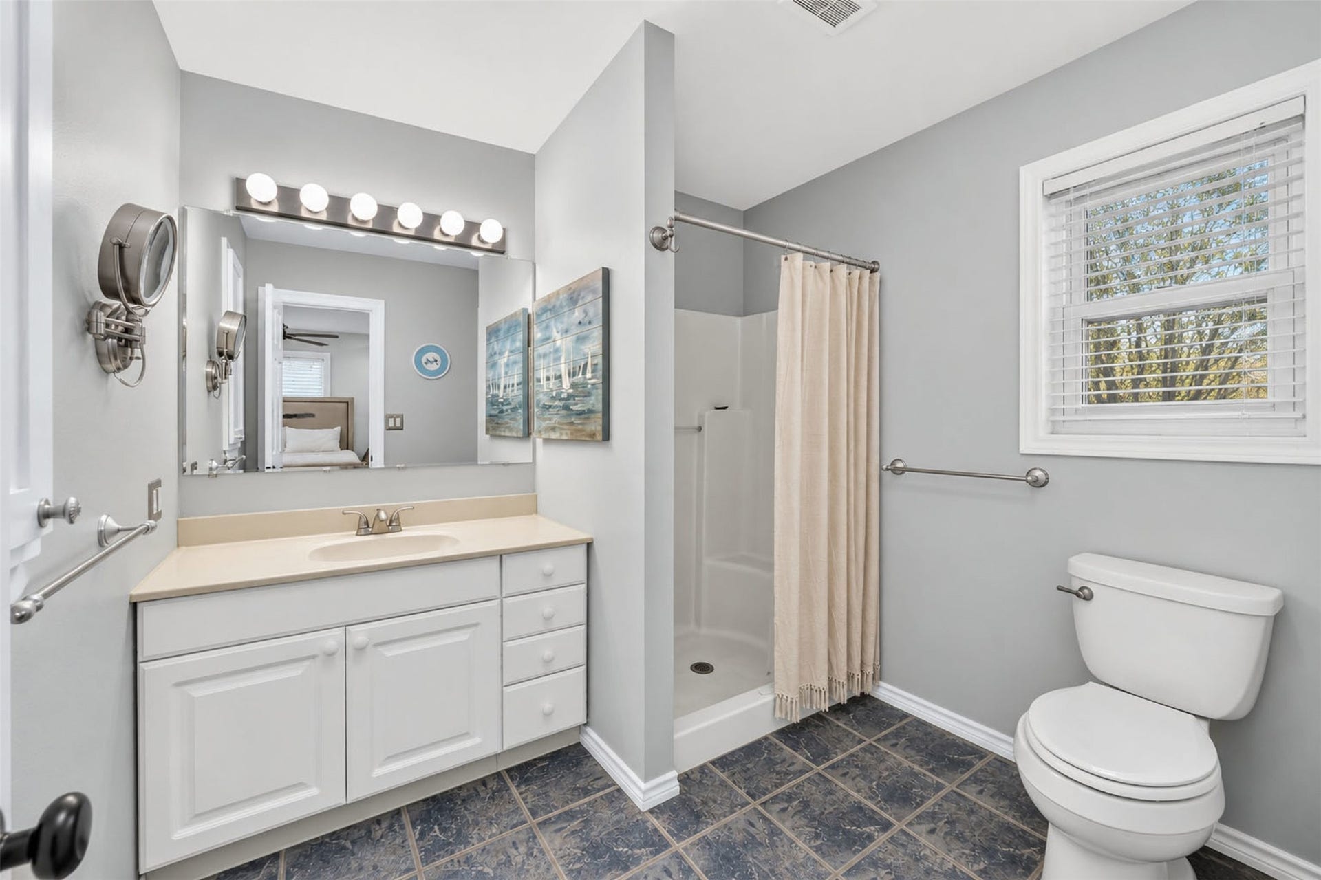 Adjoining bathroom offers a white vanity, walk-in shower, natural light, and dark tile flooring.