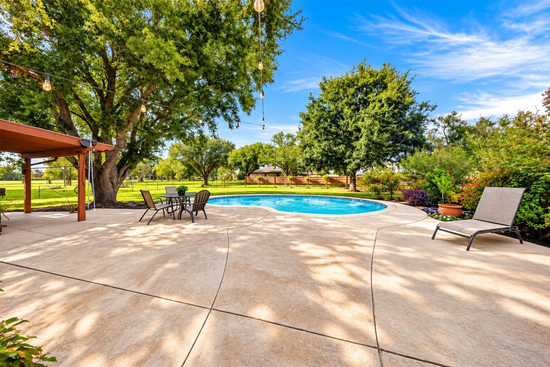 Poolside patio offers open seating areas beneath mature trees and overhead string lights.