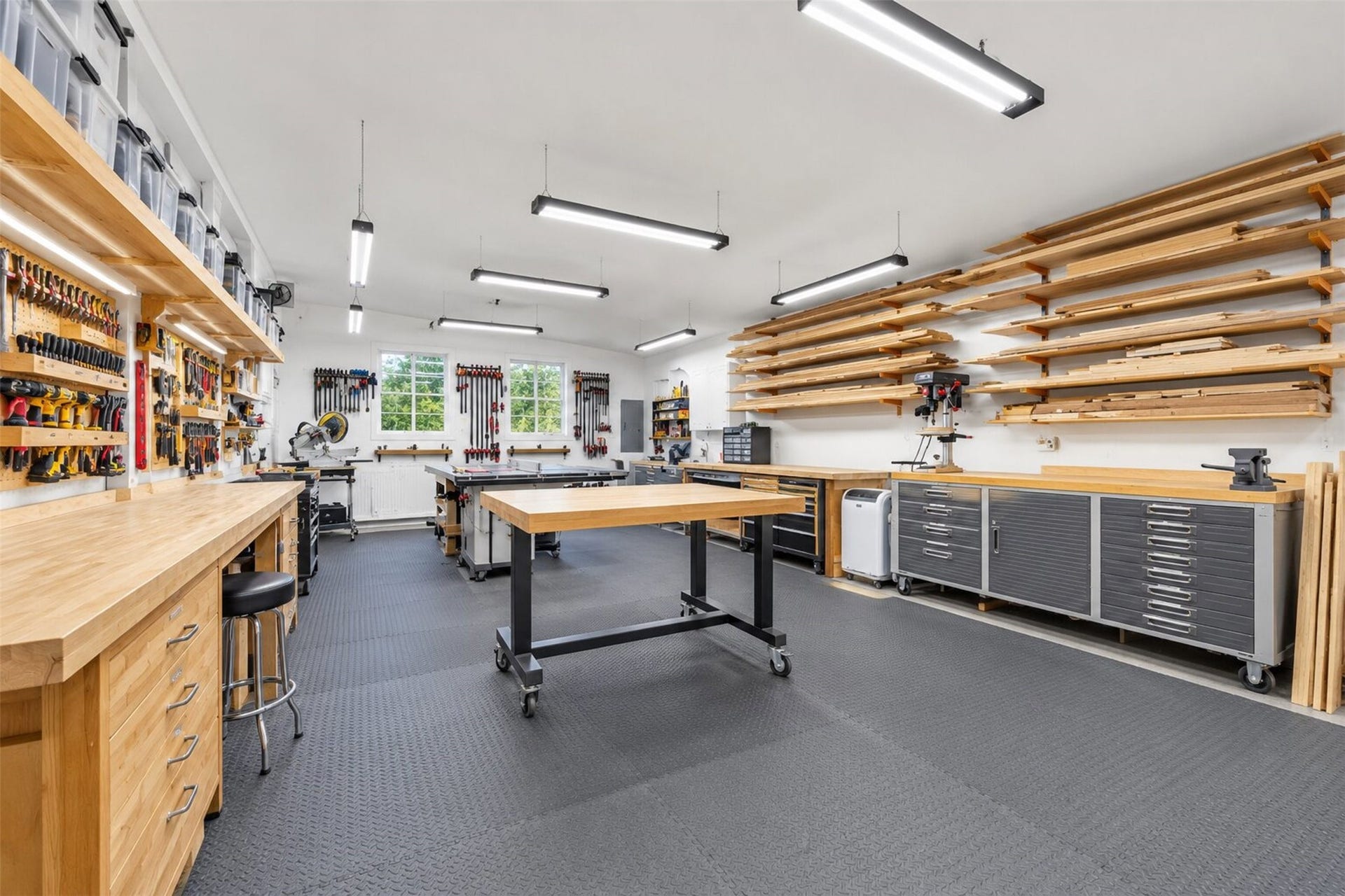Workshop arranged for woodworking, with perimeter work surfaces, wall storage, and ample overhead lighting.