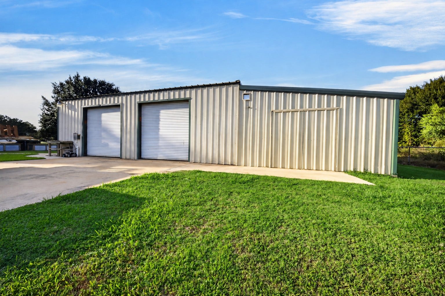 Detached metal building features two front roll-up doors and a concrete approach.