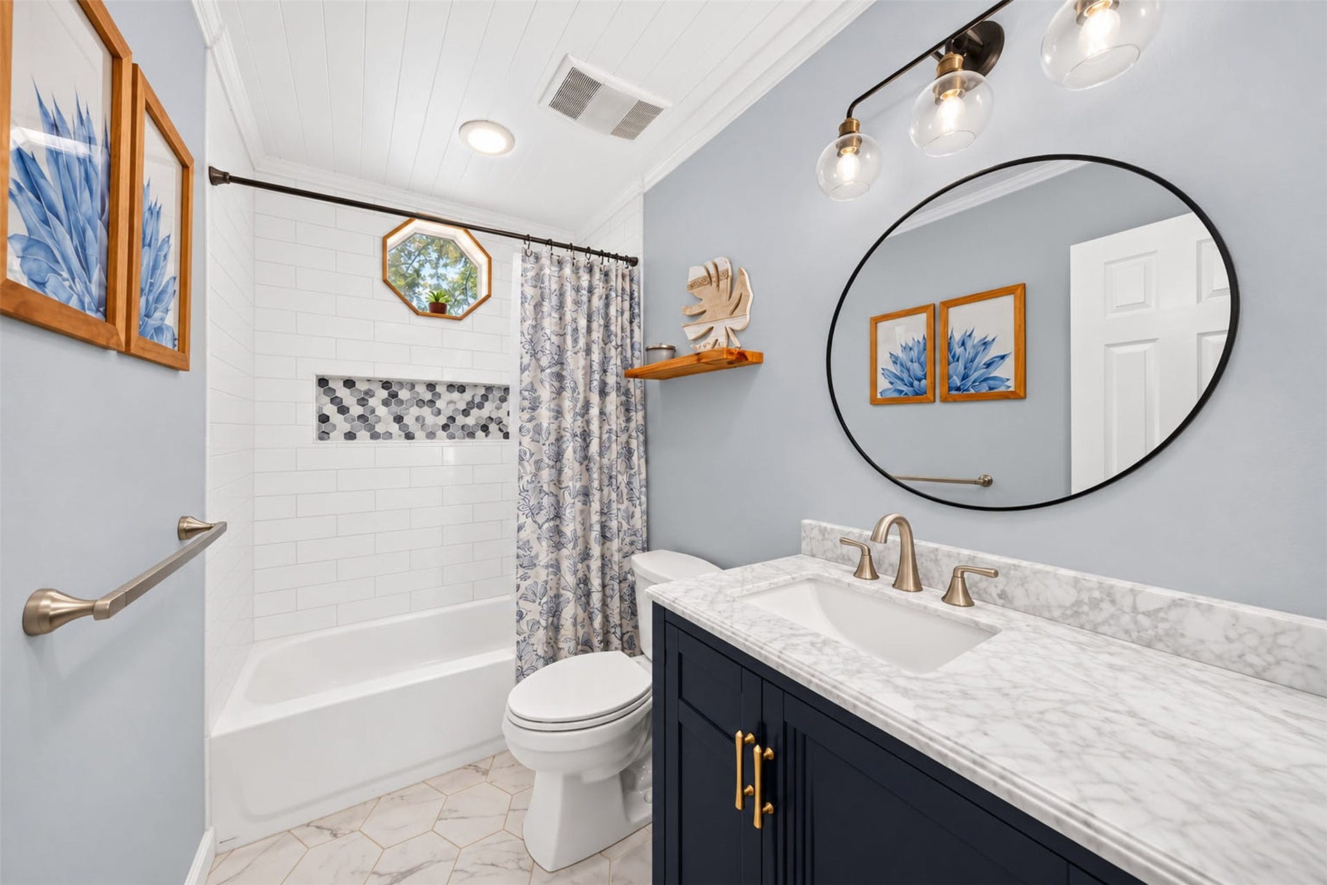 Bathroom features a navy vanity, oval mirror, and tub-shower combination with subway tile and a mosaic niche.