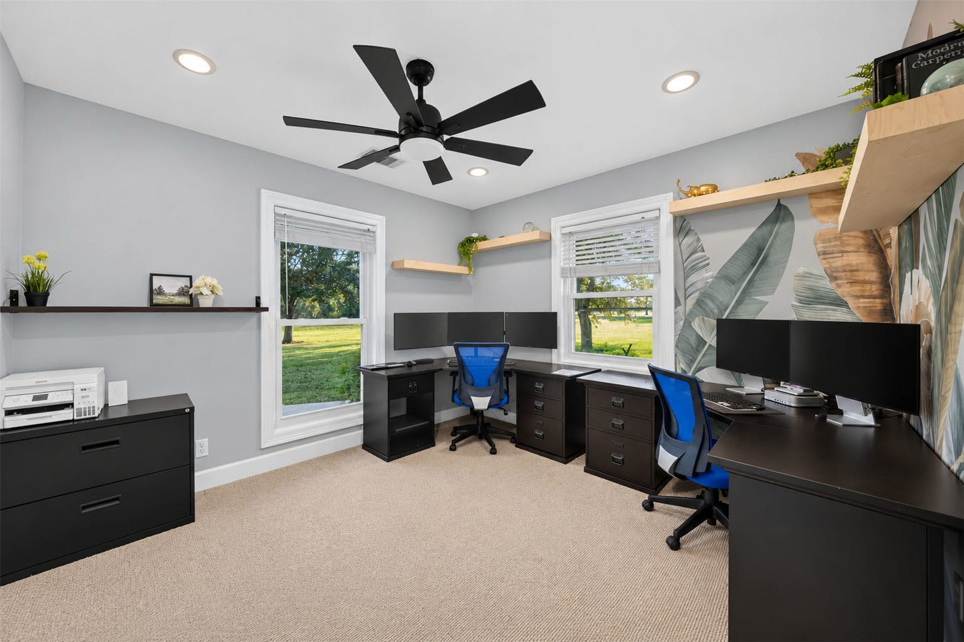 Bedroom arranged as a home office with two windows, floating shelves, a botanical accent wall, and carpet.