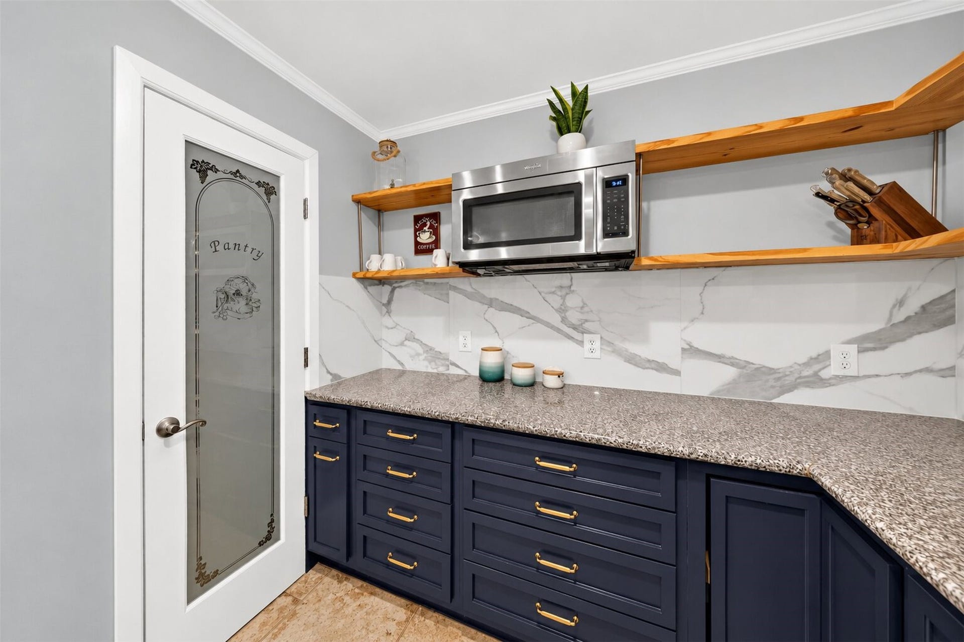 Kitchen detail highlights the decorative pantry door, open wood shelving, navy drawers, and veined backsplash.