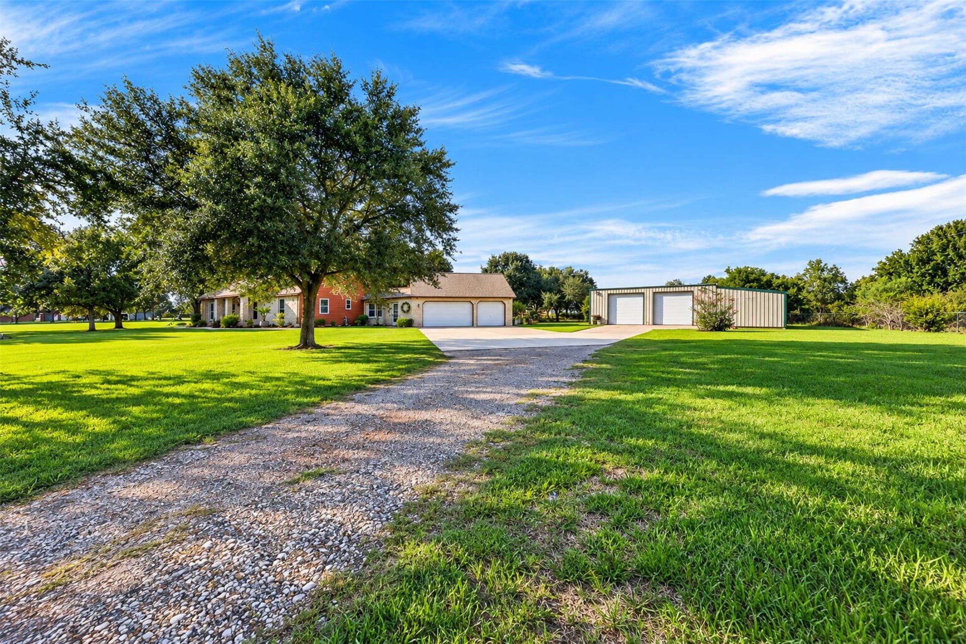 Driveway approach reveals the home, attached garage, detached metal building, and broad lawn.