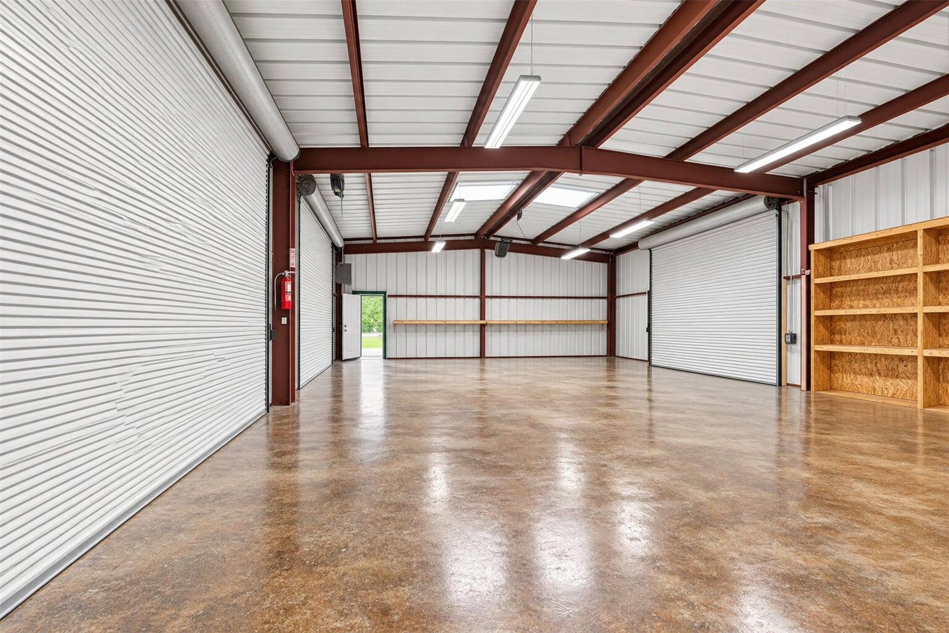 Additional workshop view shows open floor space, multiple roll-up doors, and wall-mounted shelving.