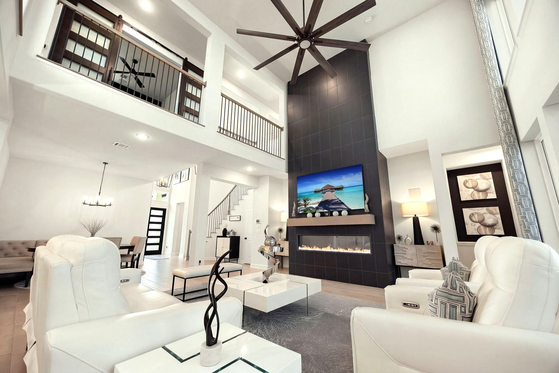 3026 Emerald Field Lane, Fulshear, TX 77423 A dramatic upward view highlights the soaring ceilings, oversized upgraded black ceiling fan, and striking floor-to-ceiling stone fireplace, complemented by elegant upstairs iron railings that enhance the home's impressive architectural design.