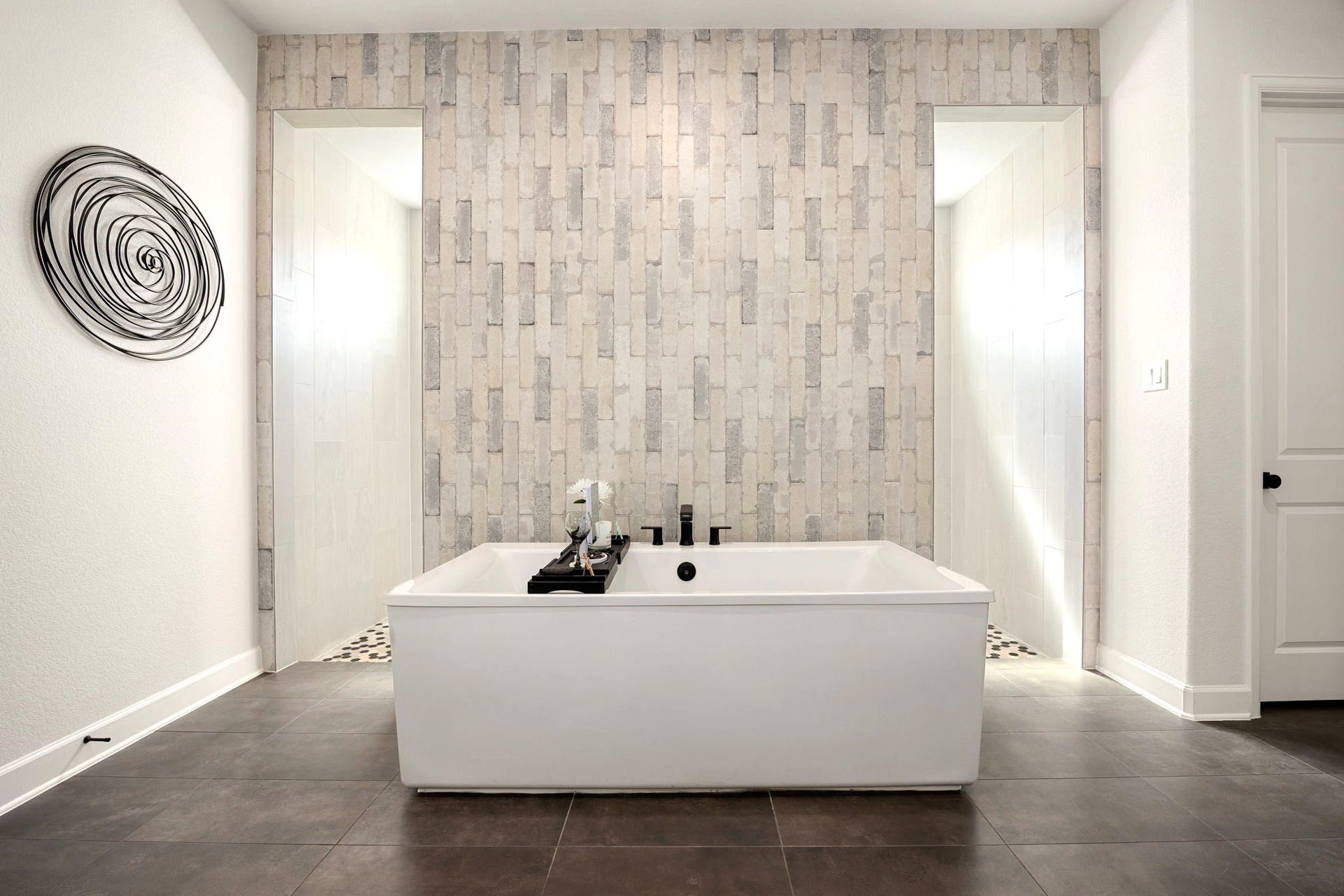 3026 Emerald Field Lane, Fulshear, TX 77423 A spa-inspired primary bath showcases an impressive double-entry shower with floor-to-ceiling custom tilework, beautifully complemented by a freestanding soaking tub positioned in front of the striking tiled feature wall for the ultimate luxury retreat.