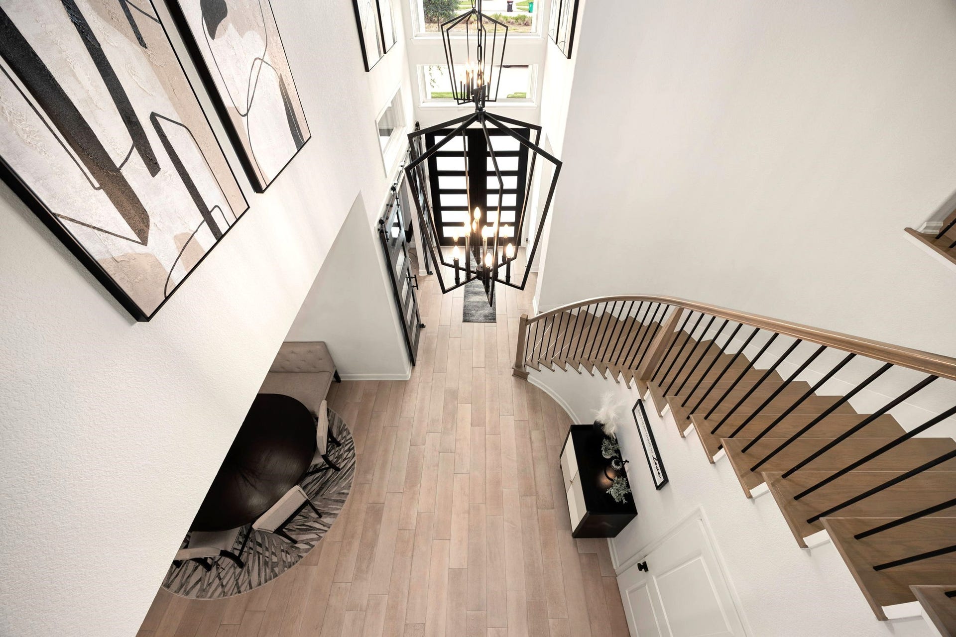 3026 Emerald Field Lane, Fulshear, TX 77423 A breathtaking second-floor perspective showcases the grand iron staircase and elegant chandelier suspended above the soaring entryway, highlighting the home's impressive architecture and dramatic two-story design.