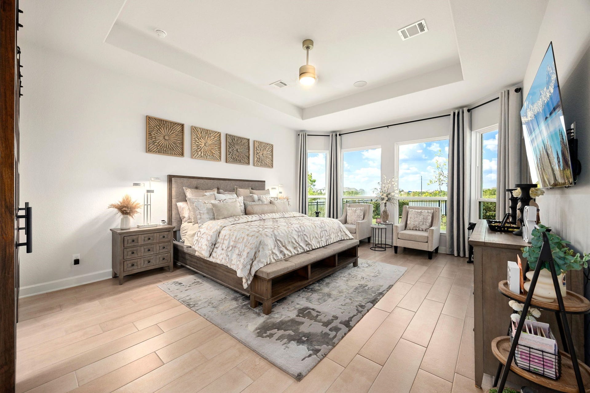 3026 Emerald Field Lane, Fulshear, TX 77423 An extended primary suite features upgraded wood tile flooring, an elegant elevated tray ceiling, and four expansive windows framing serene lake views, creating a spacious and luxurious private retreat filled with natural light.
