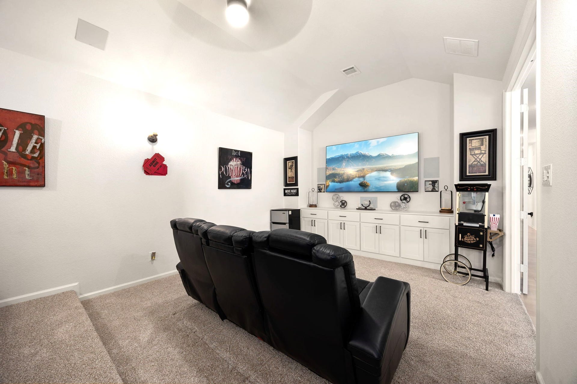 3026 Emerald Field Lane, Fulshear, TX 77423 A fully equipped home theater features custom cabinetry and drawers, built-in in-wall speakers, a popcorn machine, and a mini fridge, creating a private cinema experience designed for effortless entertaining and unforgettable movie nights.