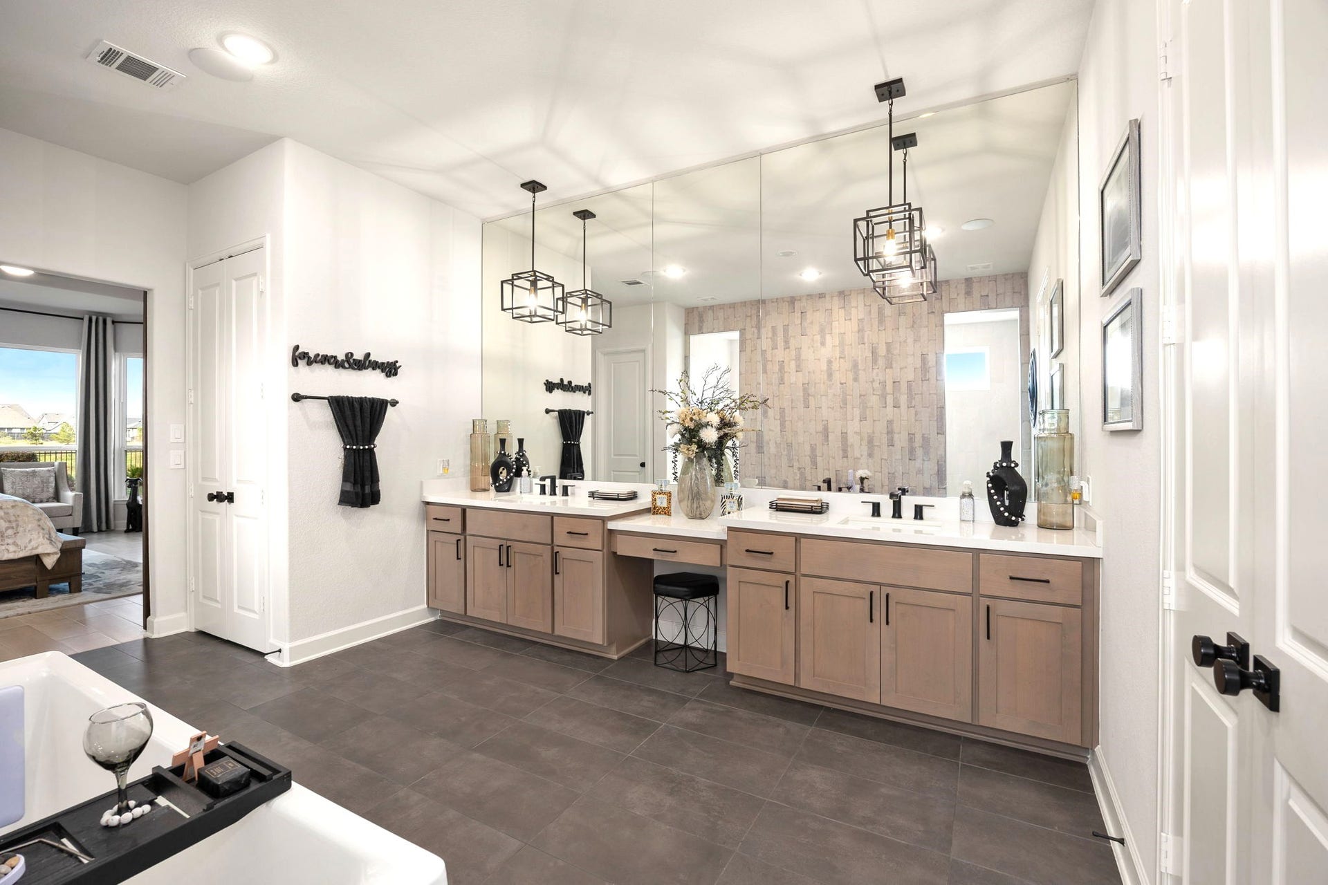 3026 Emerald Field Lane, Fulshear, TX 77423 A luxurious primary bathroom features dual vanities with upgraded cabinet hardware, elegant pendant lighting, and an expansive wall-to-wall mirror, creating a sophisticated, spa-inspired retreat with elevated finishes and timeless style.