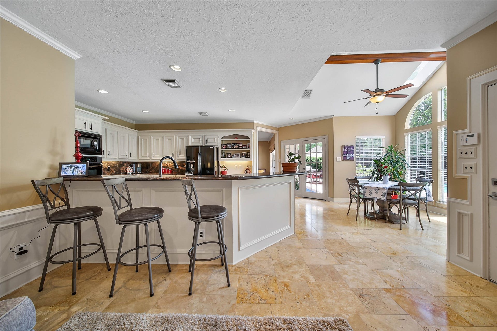 This spacious kitchen and dining area features modern appliances, a large island with bar seating, and abundant natural light from large windows. The tiled floor and neutral walls add a touch of elegance, while the open layout is perfect for entertaining.