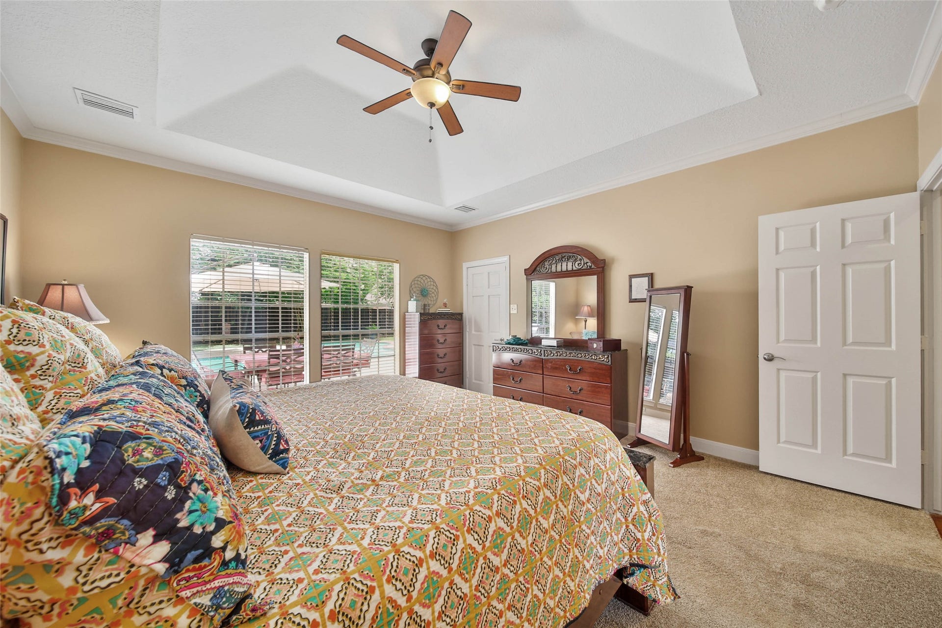 First-floor primary bedroom with generous proportions, tray ceiling and windows overlooking the outdoor living areas