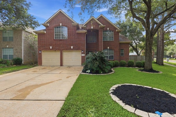 1211 Ragsdale Lane, Katy, TX 77494 Stunning two-story red brick home with charming gabled rooflines, expansive driveway, and beautifully landscaped front yard featuring mature trees and lush greenery.