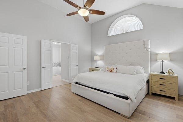 1211 Ragsdale Lane, Katy, TX 77494 Spacious bedroom with vaulted ceilings, a stylish ceiling fan, and abundant natural light from an arched window and sleek wooden flooring.