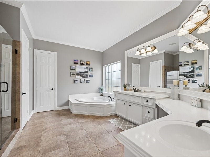 9007 Avebury Stone Circle, Missouri City, TX 77459 A luxurious primary bathroom featuring dual vanities with white cabinetry, a corner soaking tub, a glass-enclosed frameless shower, crown molding, and a frosted privacy window. A true spa-like escape within your home.