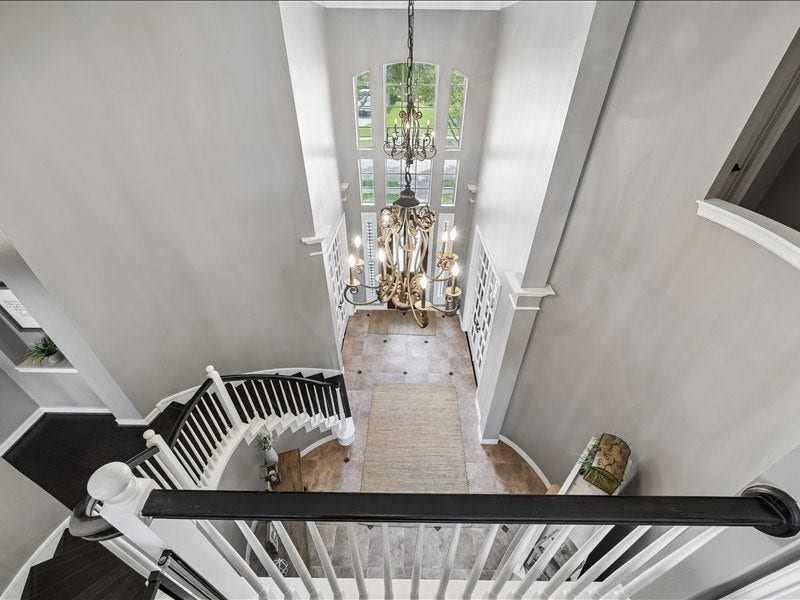 9007 Avebury Stone Circle, Missouri City, TX 77459 A dramatic overhead perspective from the upper landing reveals the sweeping curved staircase, an ornate chandelier suspended from the two-story ceiling, and the elegant arched front entry below, a true architectural centerpiece.