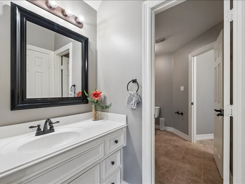 9007 Avebury Stone Circle, Missouri City, TX 77459 Secondary bathroom with a white raised-panel vanity, countertops, bronze fixtures, black-framed mirror, and a split layout offering added privacy.