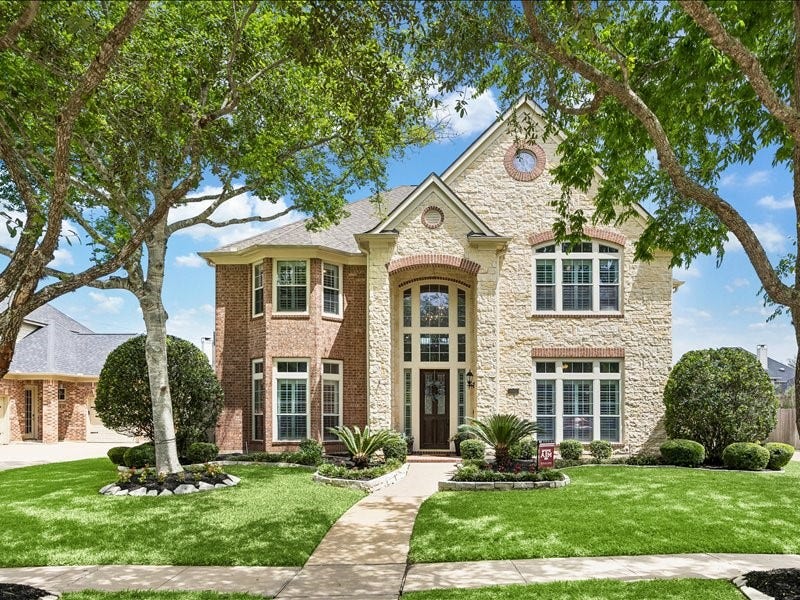 9007 Avebury Stone Circle, Missouri City, TX 77459 Stunning curb appeal defined by classic stone and brick architecture, a grand two-story facade, an elegant arched entry, manicured landscaping, and a charming walkway leading to a stately front door framed by mature shade trees.