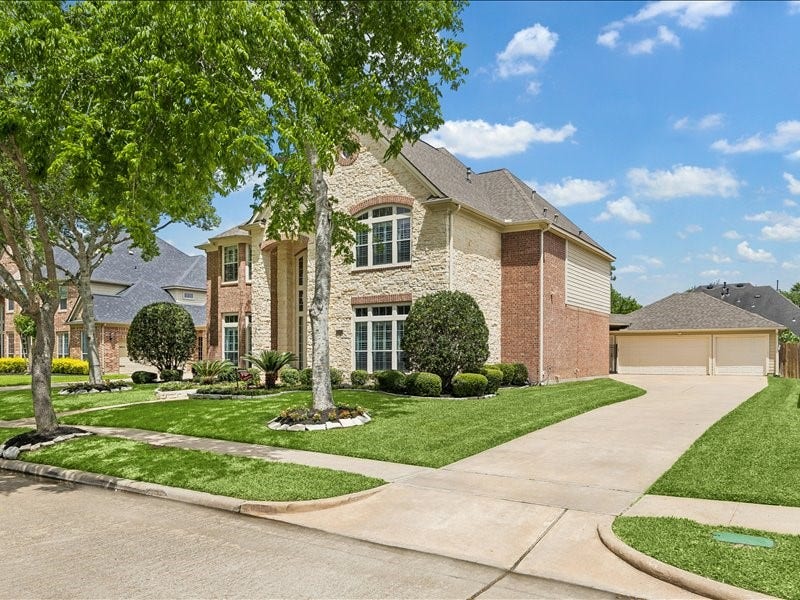 9007 Avebury Stone Circle, Missouri City, TX 77459 Angled exterior view showcasing the home's impressive two-story scale, side-entry detached 3-car garage, wide driveway, and immaculate lawn, offering a full appreciation of the property's grand presence from the street.