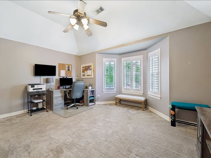 9007 Avebury Stone Circle, Missouri City, TX 77459 Versatile upstairs flex space (a secondary bedroom) currently used as a home office, featuring a bay window with plantation shutters, a cushioned window seat, ceiling fan, carpet, and ample natural light.