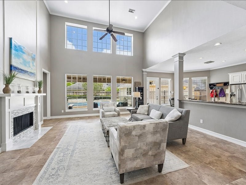 9007 Avebury Stone Circle, Missouri City, TX 77459 The expansive open-concept family room impresses with soaring two-story ceilings, oversized windows framing pool views, a stone fireplace, a stylish ceiling fan, and seamless flow into the kitchen and breakfast area. Perfect for entertaining!