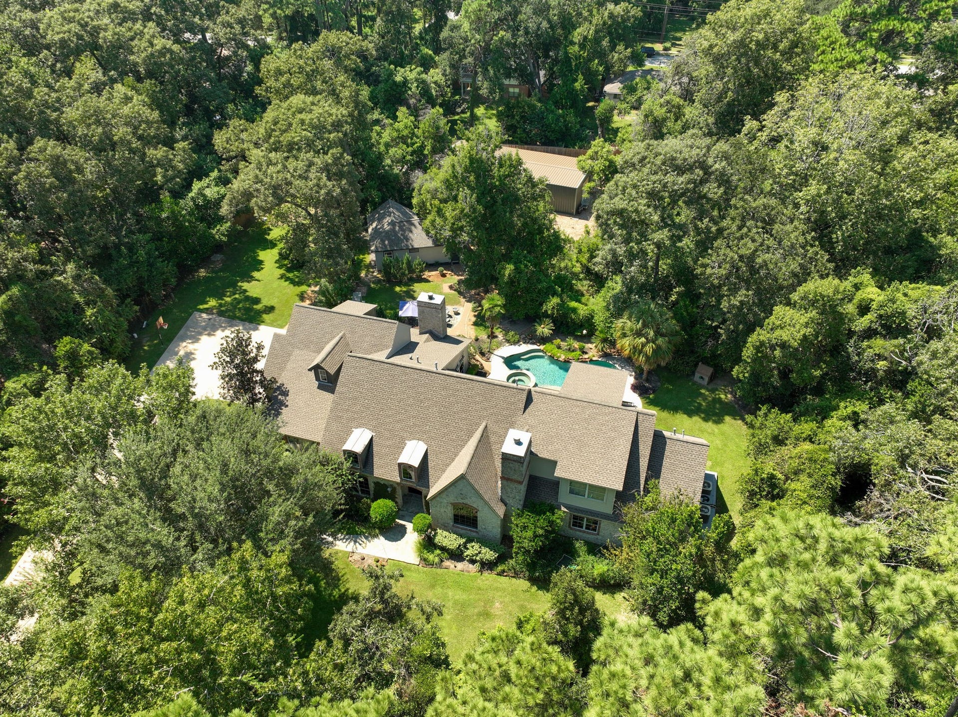 Surrounded by woods and offering exceptional privacy, this drone view showcases the one-of-a-kind property featuring the main home, guest house, pool and spa, and a spacious shop.