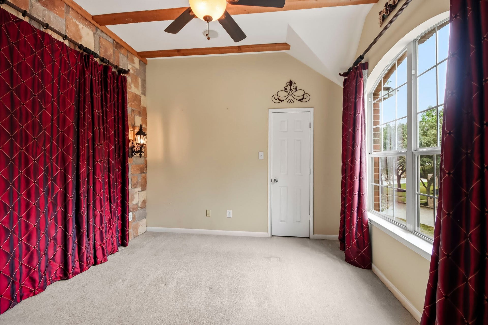 Spacious and versatile room featuring beautiful wood beam ceilings, a decorative stone accent wall, a large arched window with abundant natural light, and a closet. This room offers endless possibilities as a bedroom, home office, media room, or flex space.