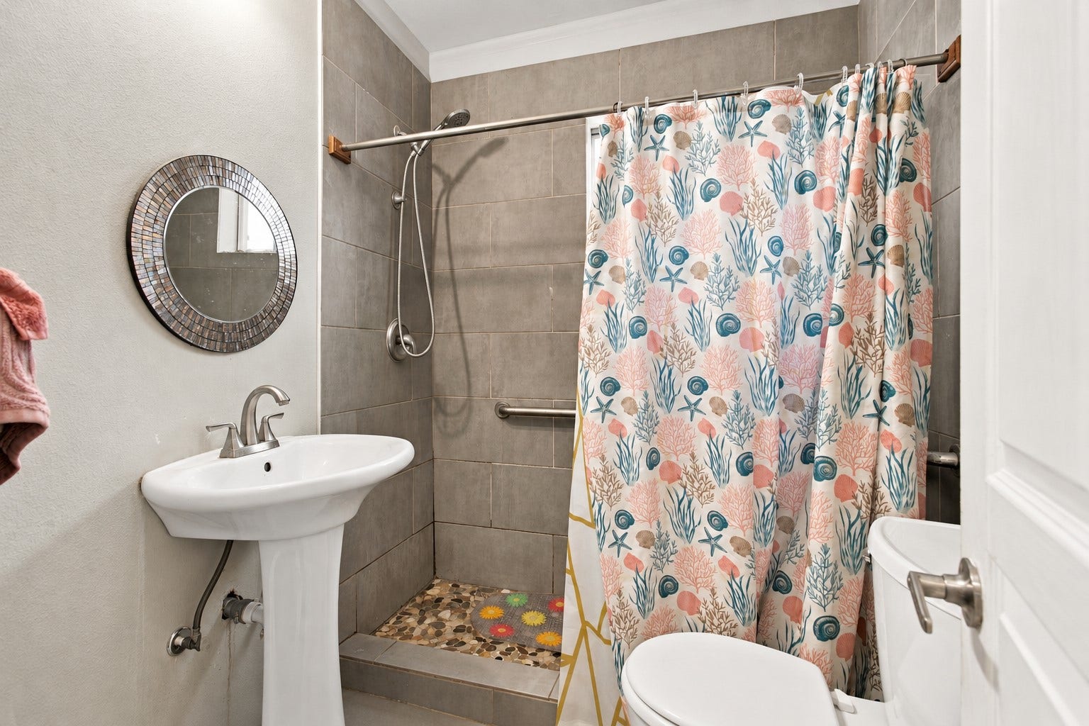 2120 Everett Street, Houston, TX 77009 Bathroom featuring gray tiled shower walls, pebble-style shower flooring, a handheld showerhead, grab bars, and a built-in shower seat with a small window for natural light (not pictured).