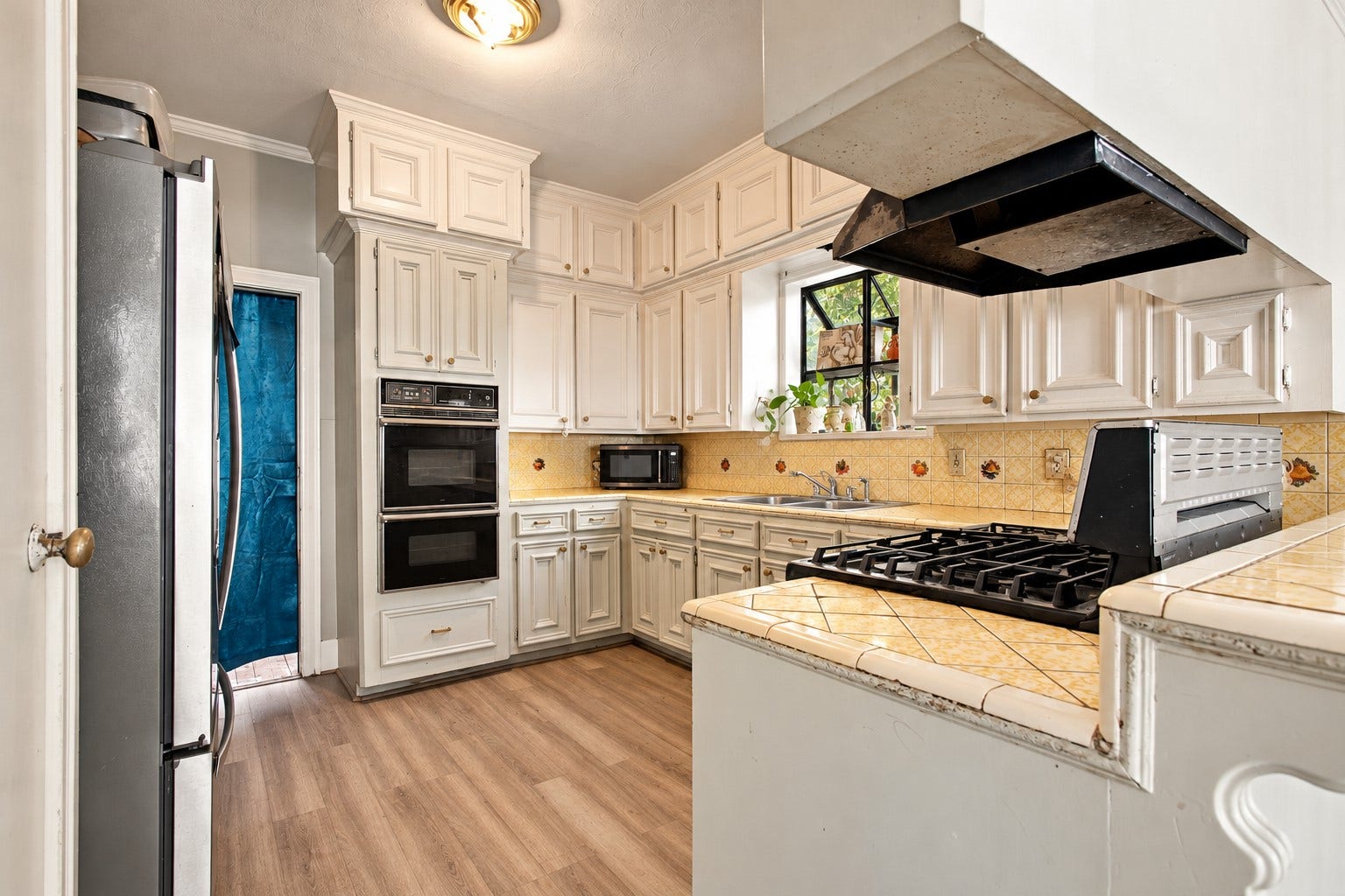 2120 Everett Street, Houston, TX 77009 Kitchen featuring white cabinetry, double wall ovens, a gas cooktop, tiled countertops, and a window above the sink, seamlessly placed between the foyer, second living space and dining room.